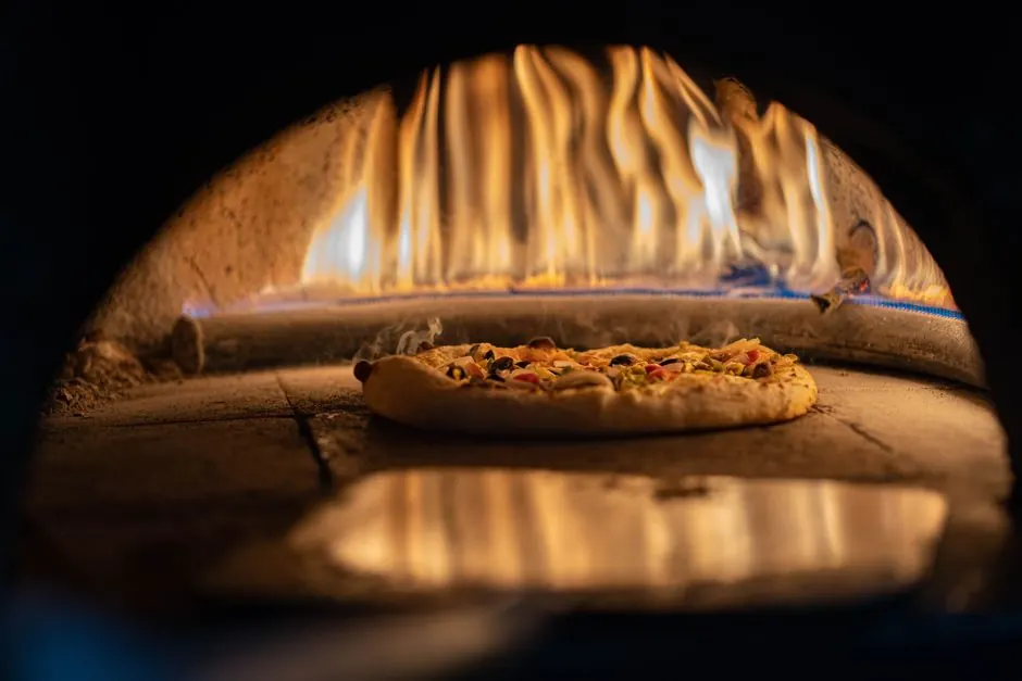 A delicious pizza baking in a traditional wood-fired oven with vibrant flames.